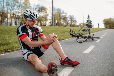 男 bycyclist 从自行车上摔下来, 撞到了膝盖, 骑自行车走上单车。运动员骑自行车
