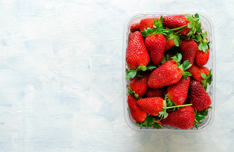 新鲜成熟的草莓在蓝色背景上用塑料盒