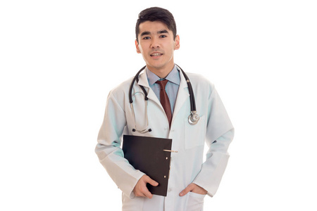 严重年轻黑发男医生穿着制服，在听诊器摆姿势孤立在白色背景上的肖像