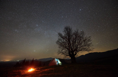 明亮的篝火在旅游照明帐篷附近燃烧.夜露营在山下美丽的星空.