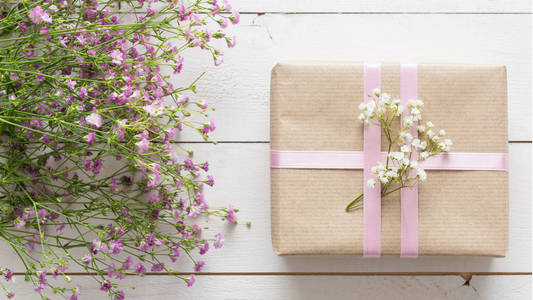 白色的木桌上粉红色的花朵和一份礼物，母亲的一天概念