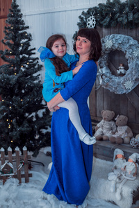 快乐妈妈与她的女儿在附近圣诞树上的长长的蓝色礼服站