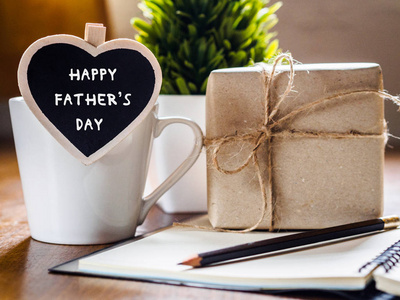 快乐的父亲日概念。咖啡杯配礼品盒, 心脏标签与快乐父亲节文本, 笔记本和眼镜在木桌背景上