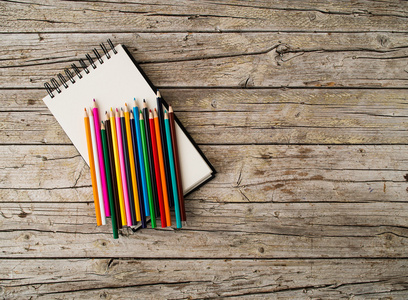 彩色铅笔蜡笔和笔记本上木制背景