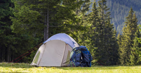 旅游营在绿色草甸与新鲜的草在喀尔巴阡山森林。露营地点的徒步旅行帐篷和背包。积极的生活方式, 户外活动, 假期, 体育和娱乐的概念
