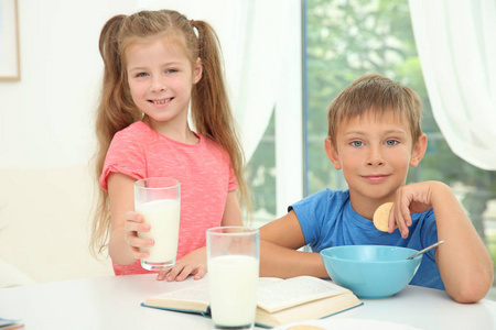 小男孩和女孩坐在桌边与牛奶和书的玻璃