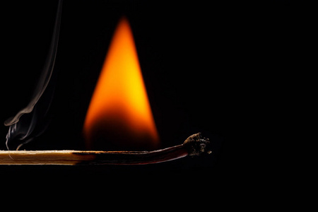 近点燃烧的木制火柴,黑色背景上有一个红色的火柴头. 近点在