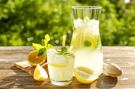 冰柠檬汁投手, 榨汁机和一杯冷柑橘饮料, 柠檬片, 薄荷叶和黄色秸秆在