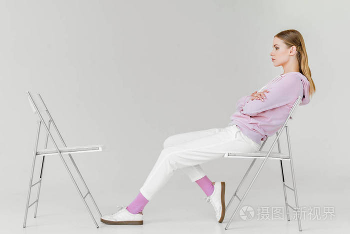 在白色的另一个空椅子前坐在椅子上有吸引力的年轻妇女的侧面视图