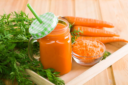 梅森罐子里放着鲜胡萝卜汁和绿稻草, 一束胡萝卜配上绿色, 玻璃杯的挤胡萝卜在木箱上轻木背。水平方向, 注重果汁