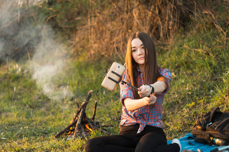 年轻漂亮的女孩在夏天坐在火边在野餐