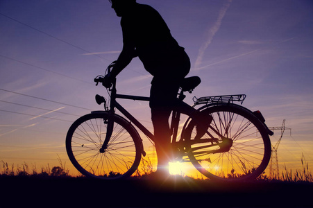 骑自行车的人开始开车。日落天空与能量场背景下的复古自行车骑手剪影