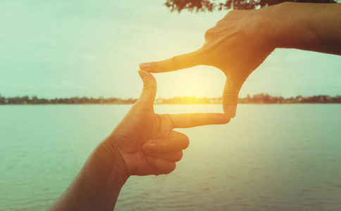 关闭女人的手做框架手势与日落照片