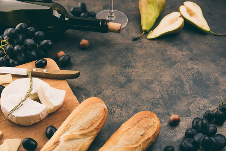 奶酪盘子里有葡萄。乳酪或乳酪在木板上。法式面包, 红酒瓶, 梨金属背景。复制空间