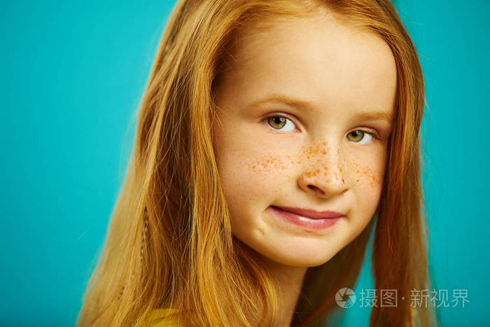 特写美丽的红发儿童女孩与可爱的雀斑在蓝色隔离