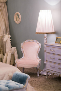 粉红色的小公主房间里有一盏落地灯, 孩子的玩具马和一个漂亮的抽屉柜, 墙上的框架。豪华卧室内饰