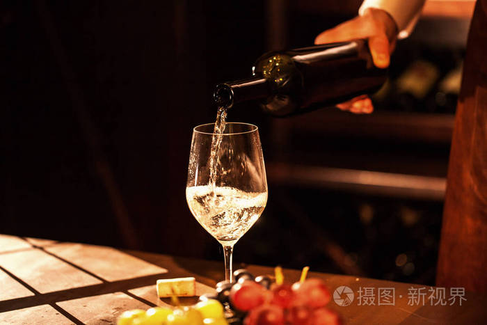 手拿着一瓶酒和倒酒入杯酒窖