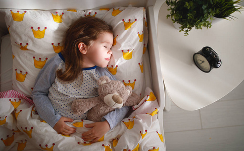 孩子的女孩睡在她的床上与玩具泰迪熊在早上