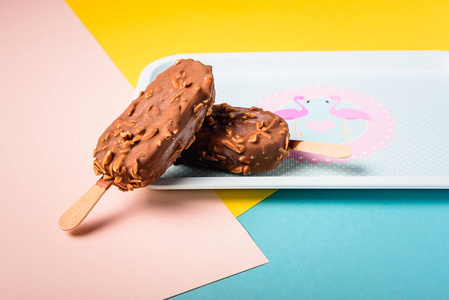 甜点巧克力冰淇淋酒吧与坚果, 木棍子在蓝色和黄色柔和的背景。爱斯基摩人在蓝色老式托盘与粉红色的 flamingosand 点。夏