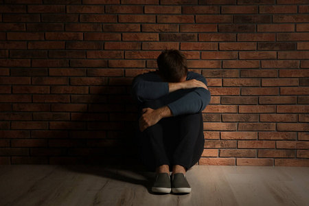 沮丧的年轻人坐在地板附近的砖墙上