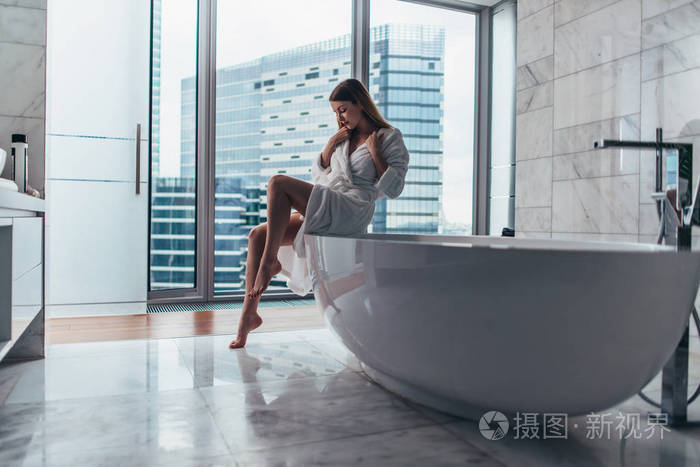 漂亮苗条的女人穿着浴衣坐在浴缸边上填满水