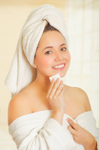 美丽微笑的年轻女子，用白毛巾捂着头部清洗她的下巴，用一块小小的纸在浴室里