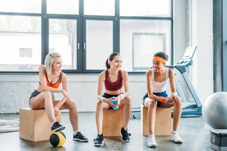 快乐的多民族女运动员互相交谈, 坐在木盒上的健身房