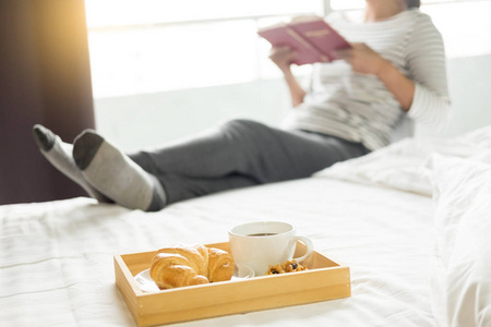 妇女读书或报纸和喝咖啡早餐在床上在早晨