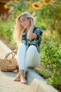 在白色长裤和绿色衬衣的美丽的年轻金发女郎的室外画像