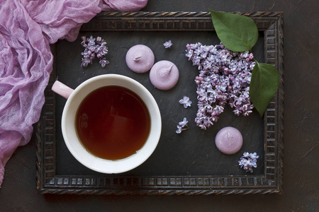 特写照片的茶杯与杏仁和美丽的新鲜丁香在框架黑色桌面背景。顶部视图