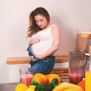 美丽的孕妇抚摸她的肚子与水果在前景