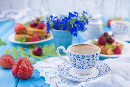 带有浆果草莓和樱桃的小蛋糕。美味的甜早餐和芳香的咖啡, 在蓝色的木质背景和花朵。复制空间