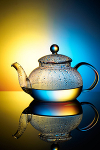 玻璃茶壶与沸腾的水和冷凝滴在光多层彩色背景上, 以逼真的反射光泽反射宏与复制空间的特写镜头
