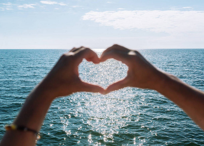 双手以心的形式向大海传递太阳束.双手塑造爱的心照片