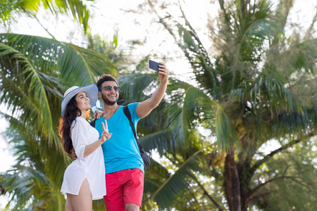 夫妇采取自拍照照片热带海滩棕榈树暑假里，年轻漂亮的人，男人女人幸福的微笑
