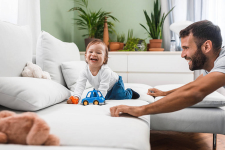 可爱的微笑白种婴儿男孩在家与他的父亲玩耍