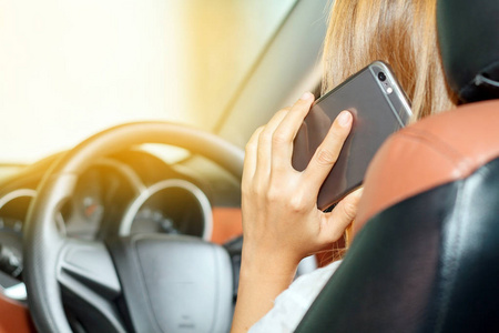 亚洲妇女驾驶汽车，在道路上使用智能手机