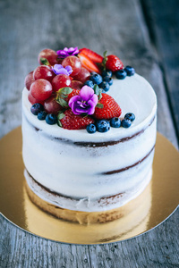 巧克力蛋糕与奶油奶油装饰草莓, 蓝莓, 葡萄和紫罗兰在一个木质的背景