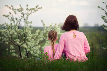 夏天的时候, 小女孩和她妈妈坐在草地上.从后面查看照片