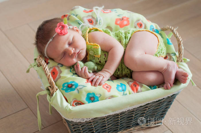 可爱的新生女婴在粉红色针织爬衣睡在一个毡绿色毯子在篮子里