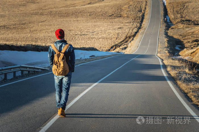 一个大胡子的时髦与老式的老式背包戴着一个红色的帽子和牛仔裤夹克和