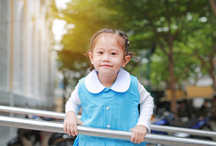 小亚洲女孩的肖像在学校制服嬉戏挂在金属楼梯上