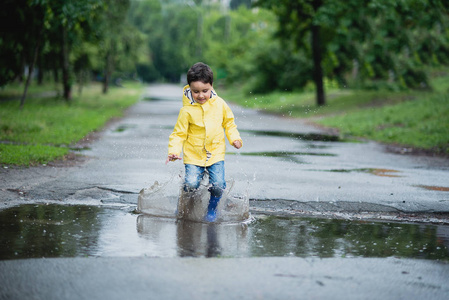 小男孩在雨衣和橡胶靴在水坑里玩