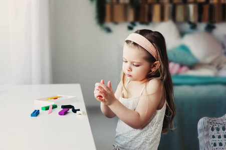 可爱的蹒跚学步的女孩玩橡皮泥或玩橡皮泥在家。孩子学习使用建模粘土