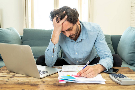 年轻的愤怒和担心的人工作与笔记本电脑在家里看账单和支付账单的家庭理财概念