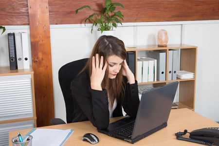 体贴疲惫的女商人坐在办公桌前看着她办公室里的电脑