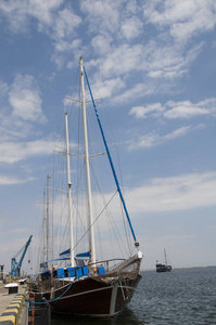远洋游艇在港口客运码头的码头上安全停泊。它有两个帆帆桅杆。木板是棕色的。在船头悬挂锚, 在开阔的海洋中停车