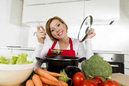 年轻快乐的家庭厨师，穿着红色围裙的女人，在家庭厨房里