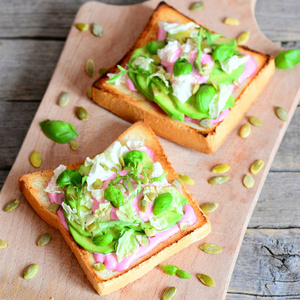 打开三明治鳄梨 生菜 罗勒 南瓜子和奶油粉色甜菜汁。在木板上的简单和健康的素食三明治。特写