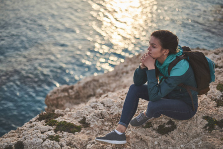 沉思的女孩坐在悬崖附近的海洋